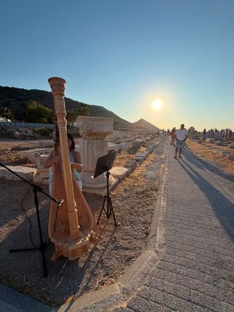 Knidos ören yerinde antik sütunların arasında arp çalan müzisyen; güneş kutsal yolun ucunda batıyor.