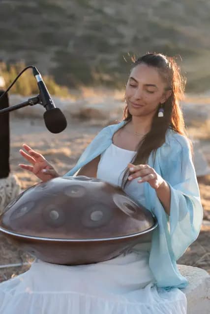 Handpan sanatçısı gözleri kapalı, elleri tasın üzerinde dolaşırken akşam ışığında kendinden geçmiş bir an.