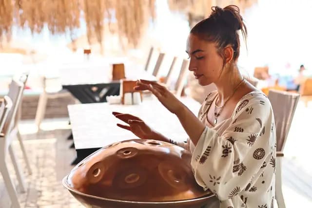 Genç müzisyen sahil sahnesinde handpan çalarken elleri enstrümanın üstünde asılı kalıyor.