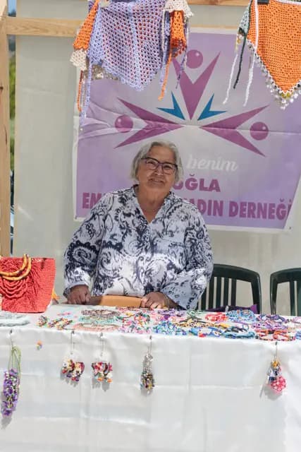 Muğla kadın derneği standındaki emektar üretici, el yapımı takılarının başında doğrudan objektife bakıyor.