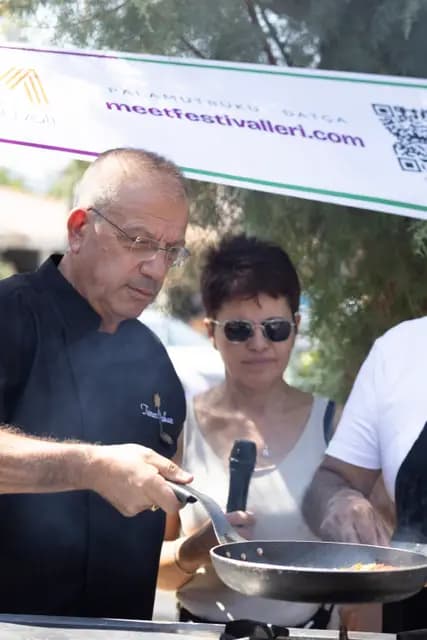 Şef tavadaki yemeği çevirirken ocaktan buhar yükseliyor.